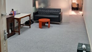 A room with a sofa, a small table, a cabinet, and a large water bottle. - Stylish and Cosy Studio with huge window view, close to Moolchand Metro Station (New Delhi)