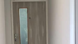A narrow hallway leading to a door with a vertical glass panel. - Stylish and Cosy Studio with huge window view, close to Moolchand Metro Station (New Delhi)