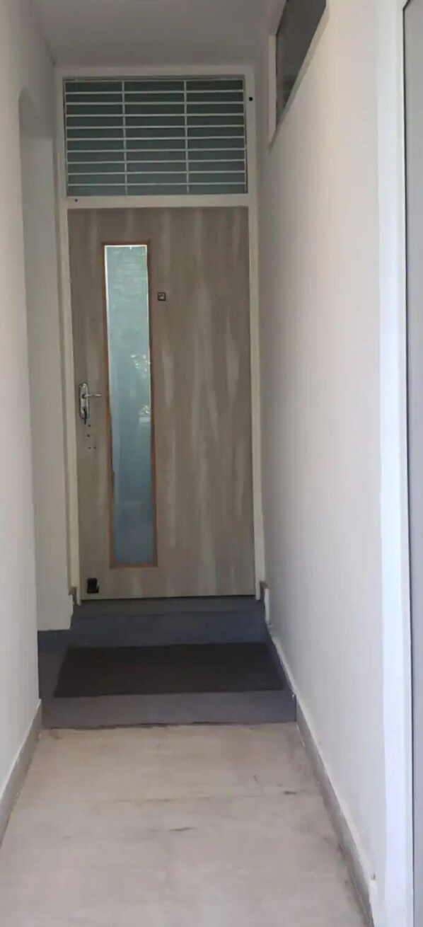 A narrow hallway leading to a door with a vertical glass panel. - Stylish and Cosy Studio with huge window view, close to Moolchand Metro Station (New Delhi)