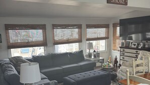 A living room with a dark blue sofa, a white side table with a lamp, a blue ottoman, a wooden dining table with chairs, and a sign that reads "JERSEY SHORE". - Lagoon Life, Beach Please! (Stafford Township)