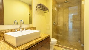 Un baño con lavamanos blanco, espejo, toallero, cabina de ducha y retrete.