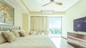 Un dormitorio moderno con una cama grande, ventilador de techo, televisor y balcón con cortinas.