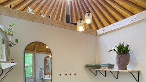 Ein Zimmer mit Holzboden, einem großen Spiegel, Regalen mit Pflanzen, einem Papierkorb und einem kleinen Tisch mit einem Korb.