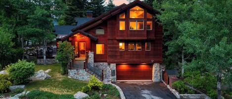 A two-story wooden house with a stone foundation, a garage, and a driveway leading to the entrance.