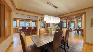 Un comedor amplio con una mesa y sillas de madera, un candelabro y vistas a la cocina y la sala de estar.