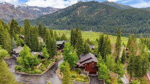 A residential area with houses surrounded by dense forests and mountains in the background.