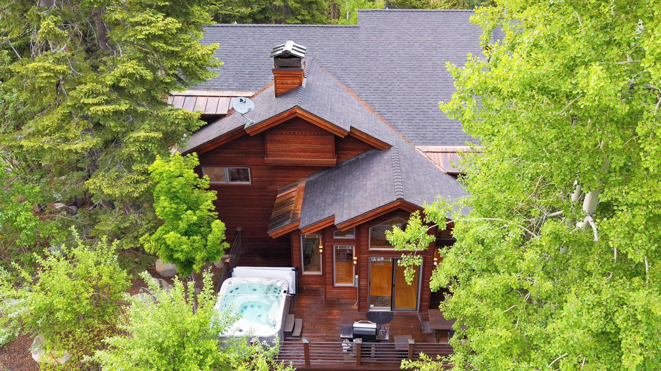 A log cabin with a hot tub, wooden deck, and a large window.
