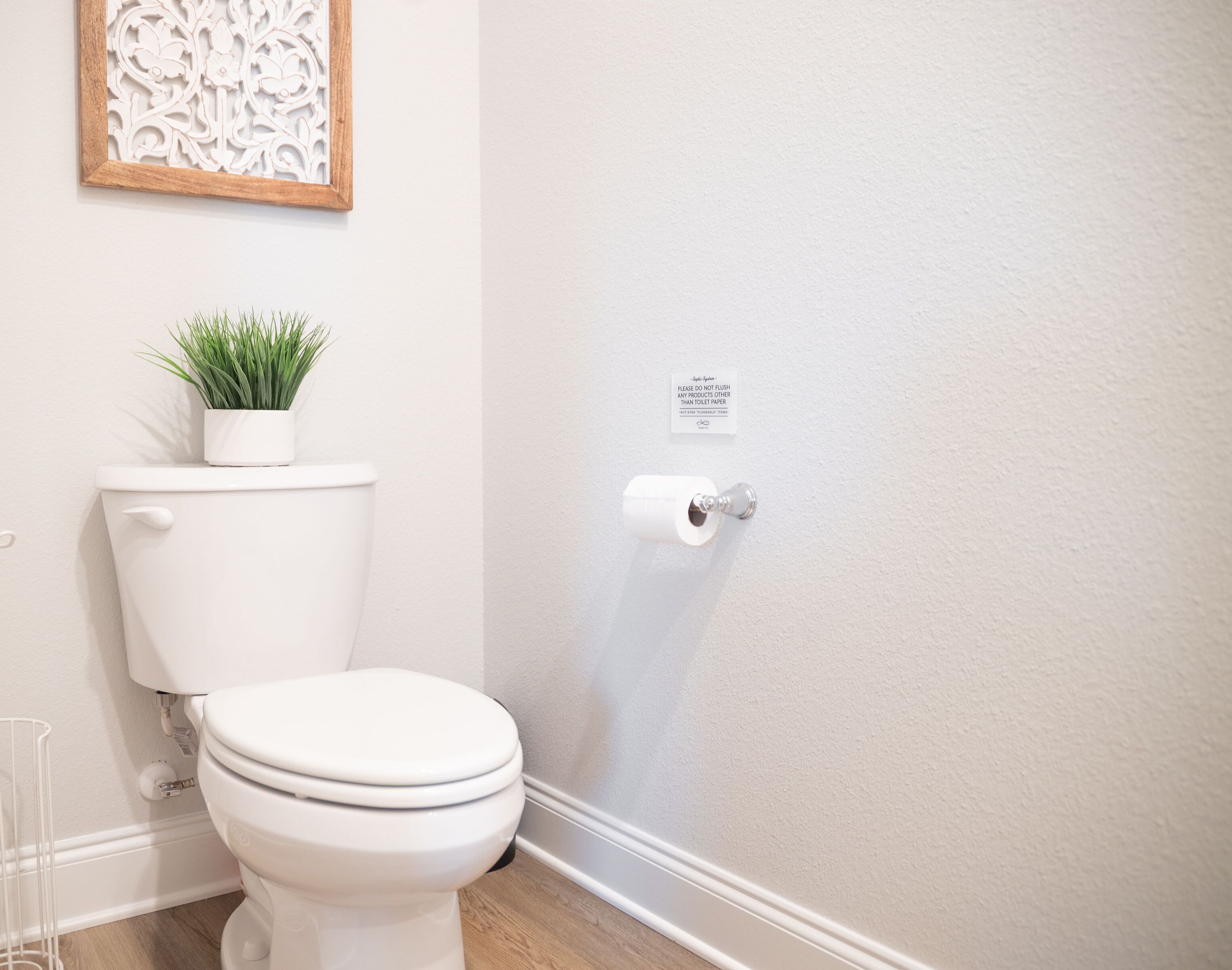 A bathroom with a toilet, a toilet paper holder, a small potted plant, and a decorative wall piece.