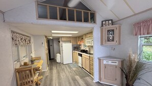 Una cocina amplia con armarios de madera, un refrigerador y un microondas. Hay un comedor con mesa y sillas, y una ventana con cortinas.