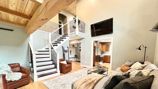 Un vaste espace de vie avec un escalier menant à l’étage supérieur, un canapé gris et un plancher en bois.