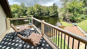 Un balcon agrémenté de meubles en osier, d’une petite table et offrant une vue sur un lac et des arbres.