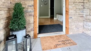 Une façade en pierre avec une porte en bois, un arbre en pot, des bougies, des lanternes et un paillasson.