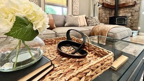 Un salon moderne avec une table basse en verre, un vase de fleurs blanches et une cheminée en arrière-plan.