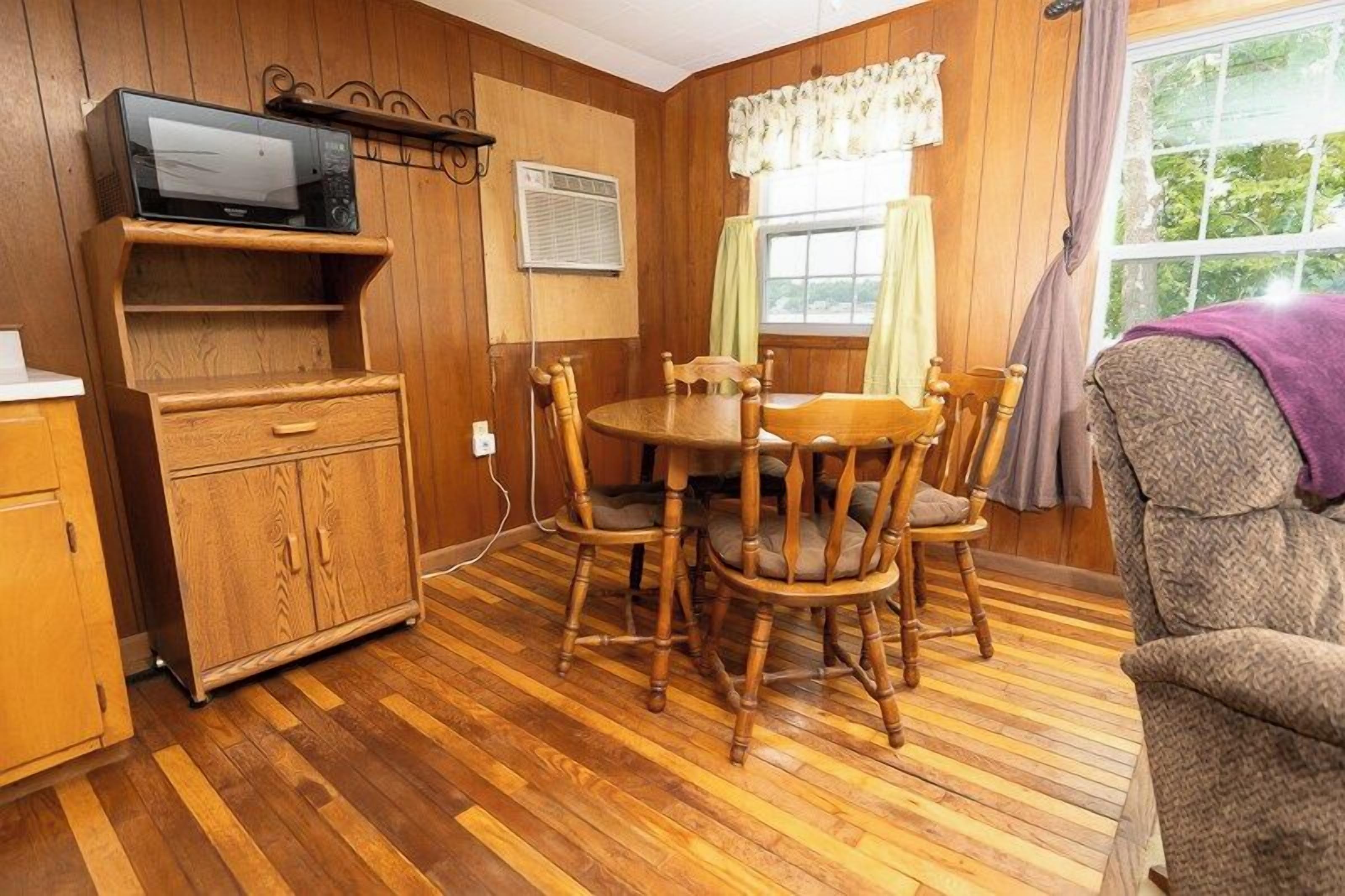 A wooden-paneled room with a dining table and chairs, a cabinet, and a television on a shelf.