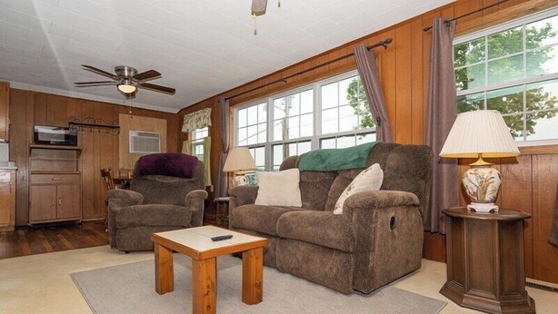 A living room with a sofa, armchairs, a coffee table, and a lamp. There is a window with curtains and a ceiling fan. - The Cabin at Prairie Hollow Camp w/ Boat Slip* (Roach)