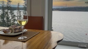 Ein Tisch mit einem Glas Weißwein, einem Teller mit Speisen und Blick auf einen See durch ein Fenster.
