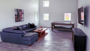 Ein modernes Wohnzimmer mit einer Eckcouch, einem Couchtisch, einem Billardtisch und einem flachbildfernseher an der Wand.