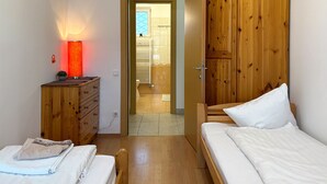 A bedroom with a wooden wardrobe, a bedside table with a lamp, and a view into the bathroom.