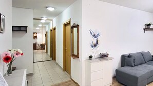 A modern living room with a grey sofa, a white side table, and a mirror. There is a hallway leading to a kitchen area.
