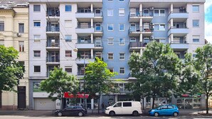 A multi-story residential building with balconies, a visible storefront, and parked cars.