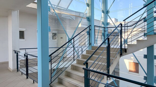 A modern interior with a staircase, glass ceiling, and metal railings.