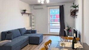 A modern living room with a grey sectional sofa, a dining table with chairs, and a wine bottle.