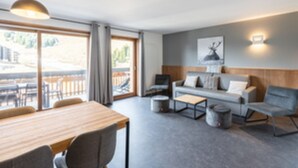 A modern living room with a sofa, a dining table, and a large window. - Residence Les Ecrins D'auris (Auris)