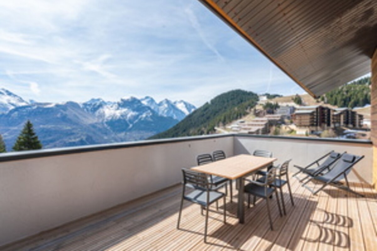 A wooden deck with a table and chairs, overlooking a mountainous landscape.