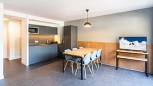 A modern kitchen with grey cabinets, a wooden dining table, and a TV on the wall. - Residence Les Ecrins D'auris (Auris)
