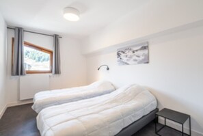 Een kamer met twee bedden, een raam met gordijnen, een wandlamp en een klein tafeltje.