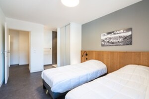 Quarto de hotel com duas camas, cabeceira de madeira, um quadro na parede e uma porta que dá para outro cômodo.