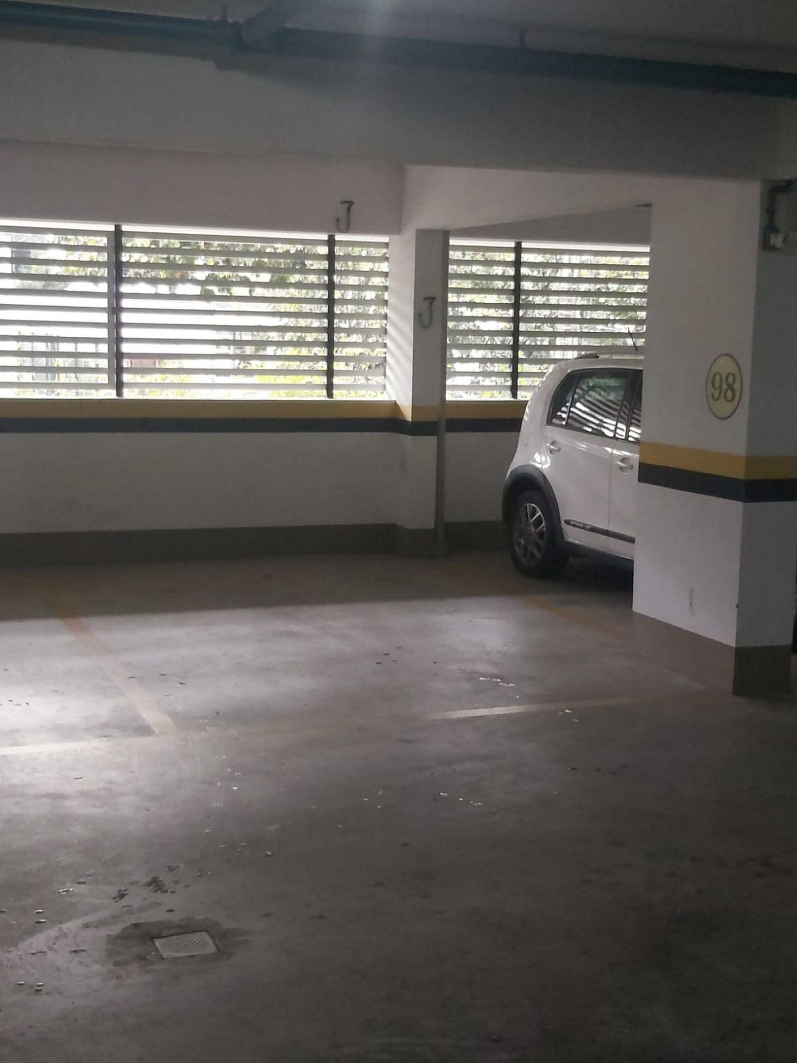 Un estacionamiento con pisos de concreto, paredes blancas y un auto blanco estacionado en uno de los espacios.