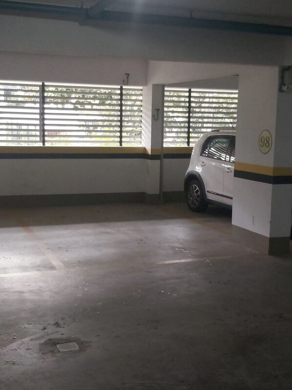 Un estacionamiento con pisos de concreto, paredes blancas y un auto blanco estacionado en uno de los espacios.