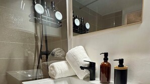 Un baño con un lavamanos blanco, un espejo, una toalla y una botella de jabón.
