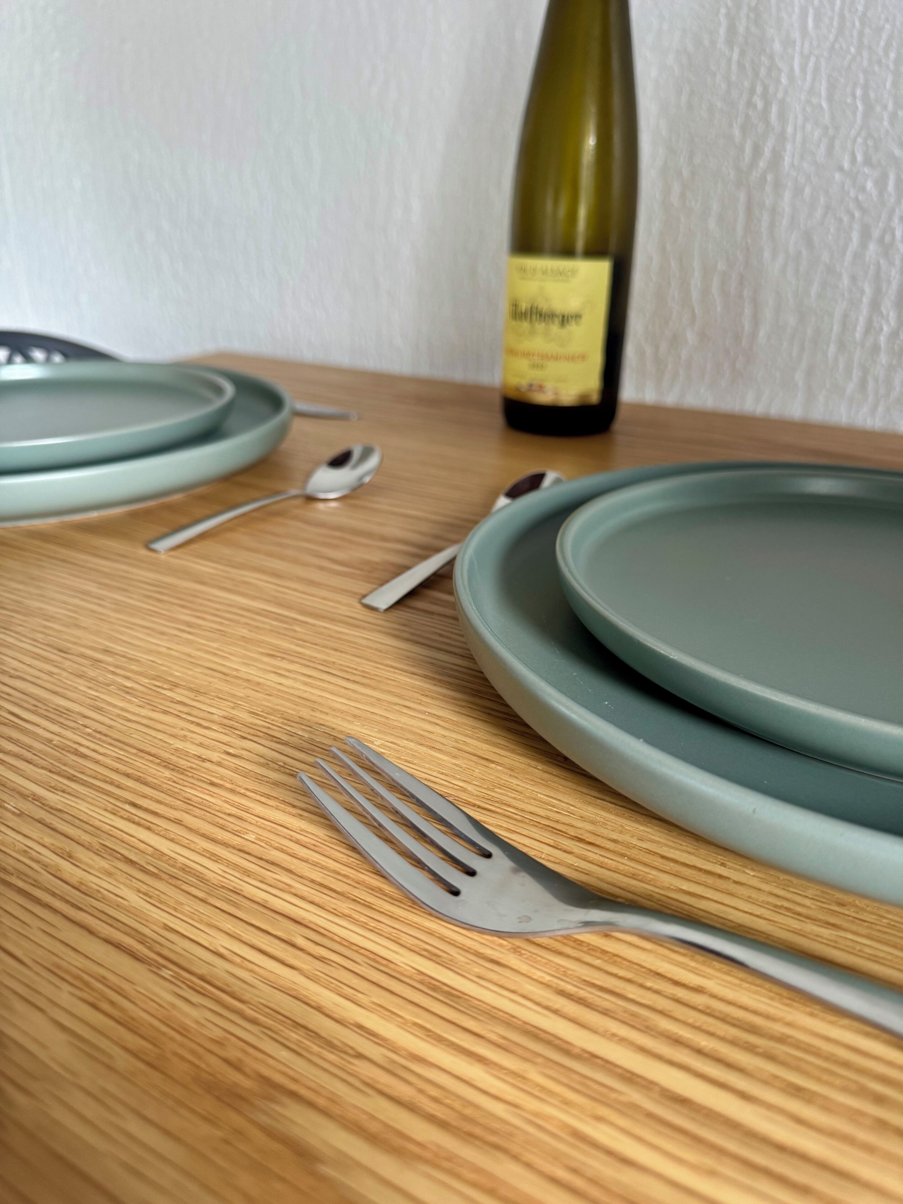 A wooden table with a green plate, a fork, and a bottle of wine in the background.