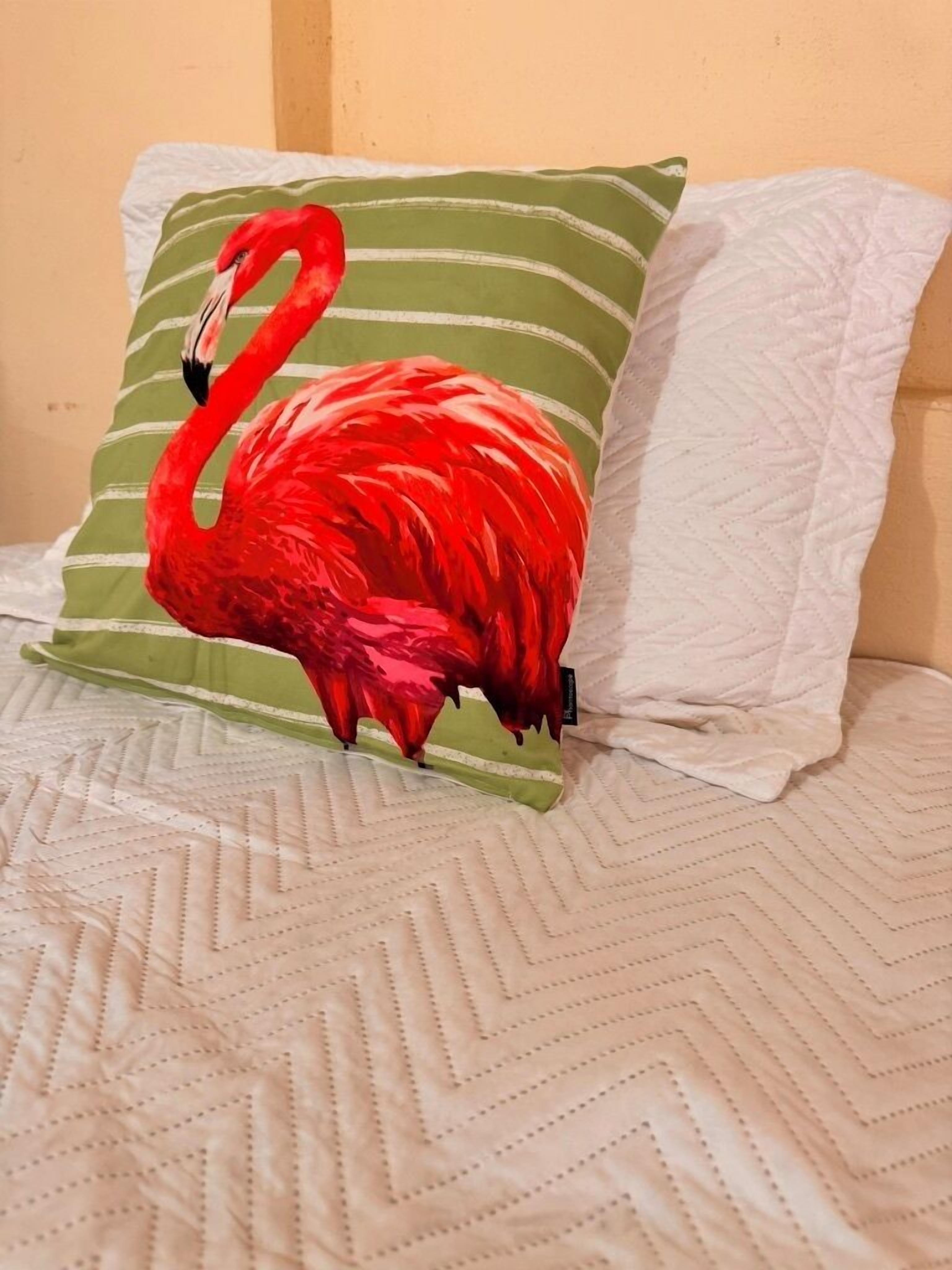 Una cama con colcha blanca y almohada con diseño de flamenco.