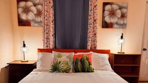 A bedroom with a bed, two nightstands, a wooden shelf, and two wall-mounted lamps. - Casa Sunset (El Tránsito)