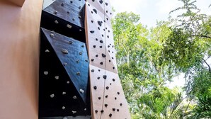 A climbing wall with various holds and a pathway leading to a seating area surrounded by greenery. - Resort-Style Loft in AfloraTulum (Tulum)