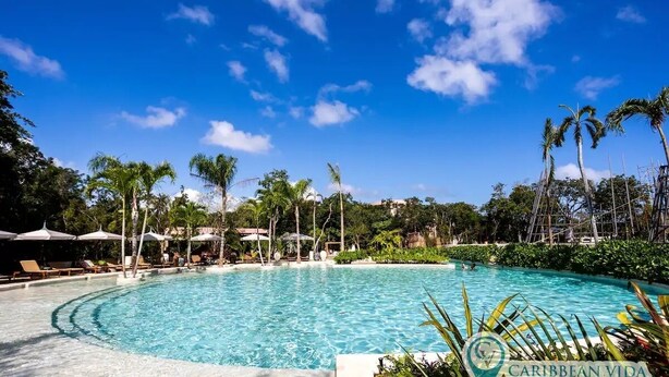 A large outdoor swimming pool surrounded by palm trees and lounge chairs under a clear blue sky. - Resort-Style Loft in AfloraTulum (Tulum)