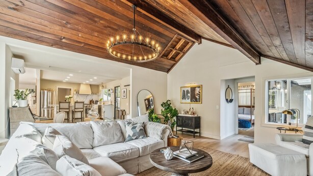 Ein geräumiges Wohnzimmer mit einer großen Eckcouch, einem runden Couchtisch und einer Holzbalkendecke.