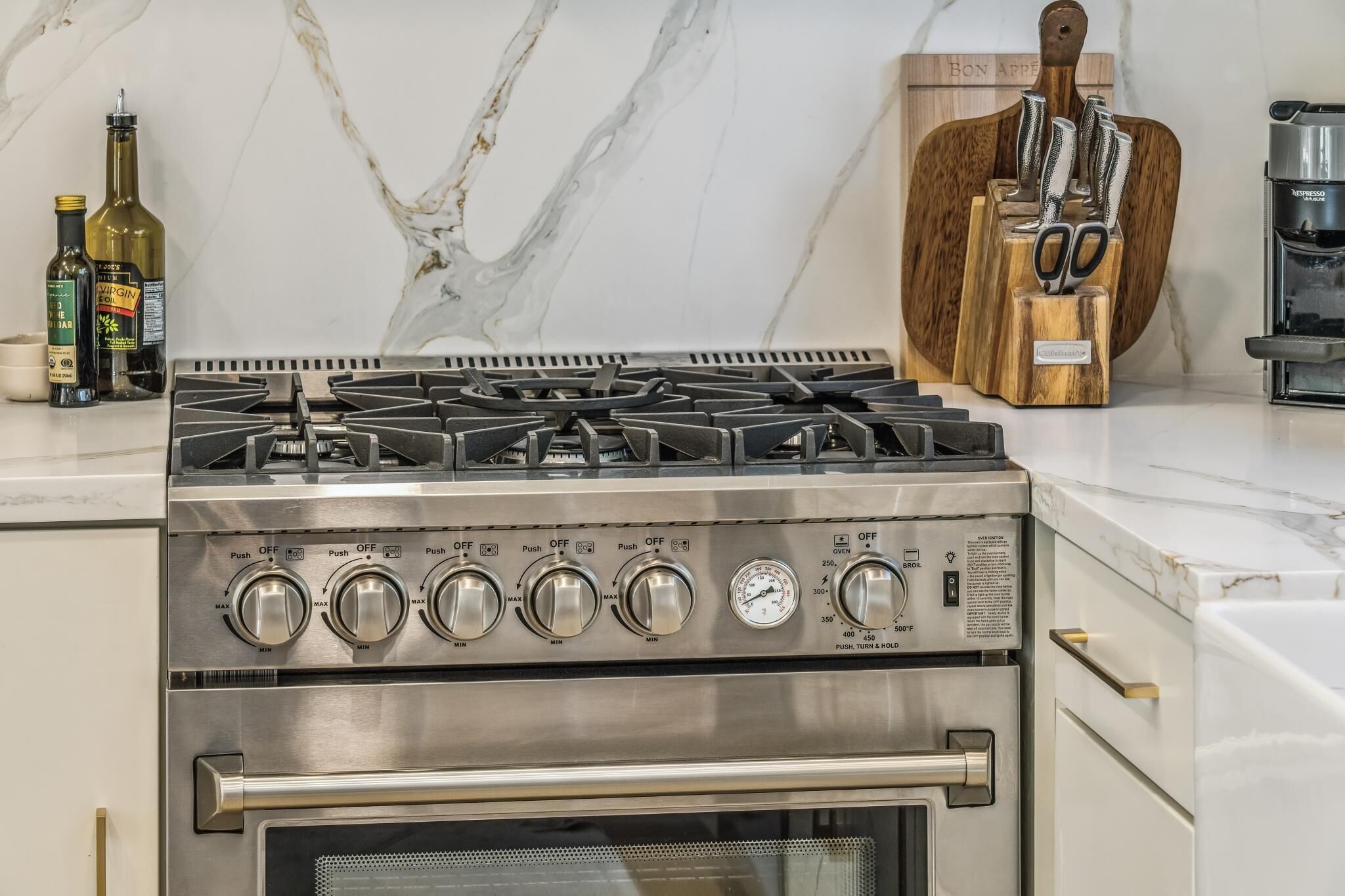 Una cocina con estufa a gas de acero inoxidable, horno y encimera de mármol.