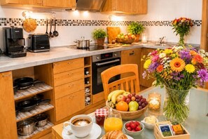 A kitchen with a coffee maker, toaster, and various kitchen utensils. There is a fruit bowl, a vase with flowers, and a candle on the counter.