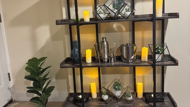 Un estante de madera con varios niveles y diversos objetos decorativos, como velas, plantas y recipientes de metal.