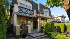 Une maison à deux étages, avec un toit sombre, un balcon et un jardin bien entretenu.