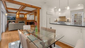 Une cuisine moderne avec des meubles blancs, une table à manger en verre et des poutres en bois.
