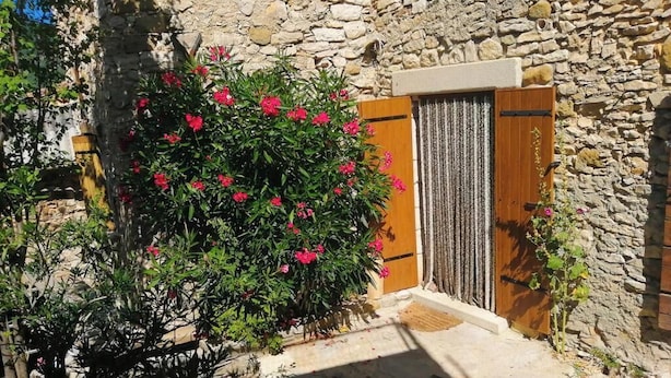 Un edificio de piedra con puerta de madera y un pequeño jardín lleno de flores rosadas.