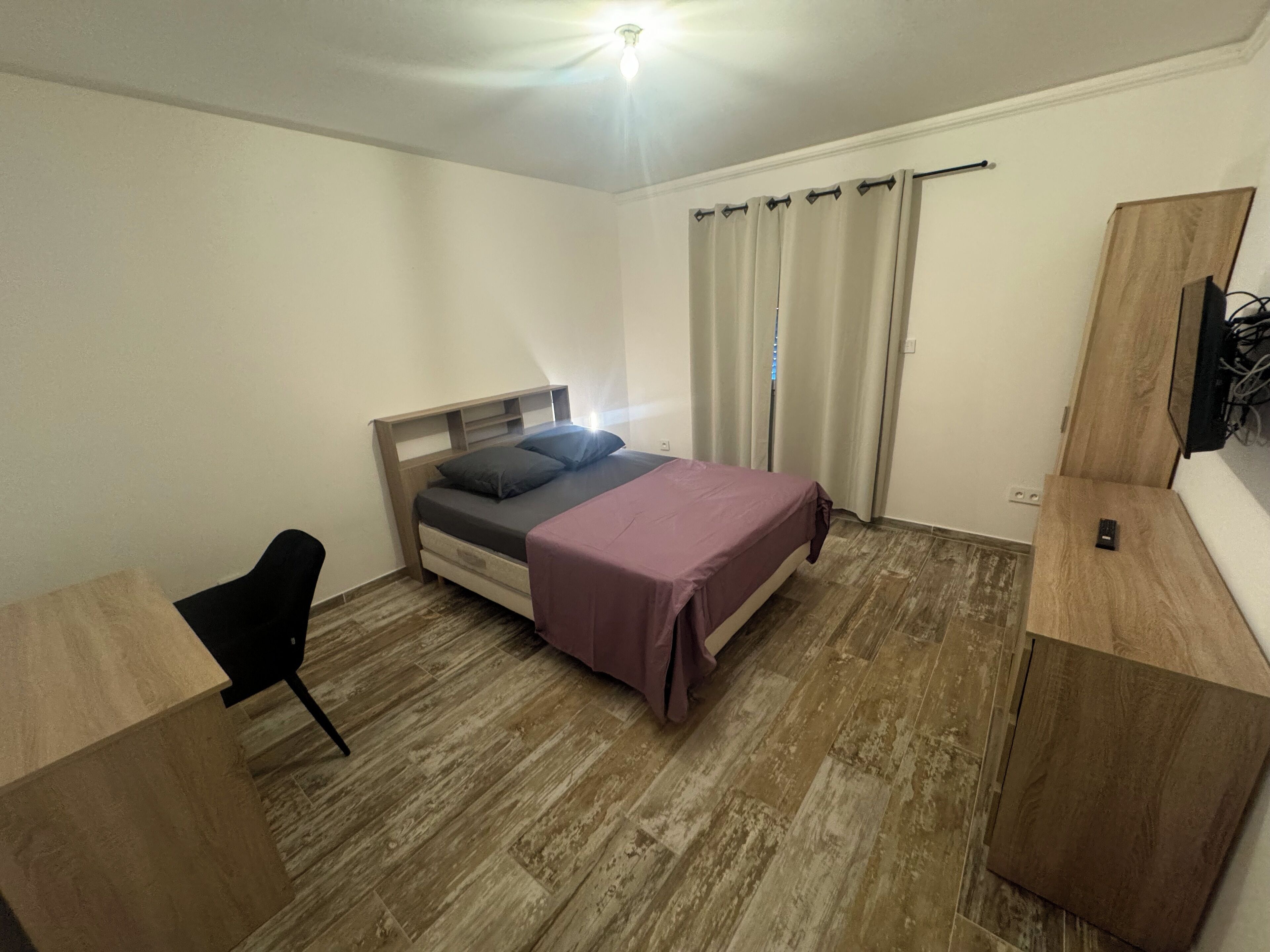 A bedroom with a bed, a desk, a chair, and a TV mounted on the wall.