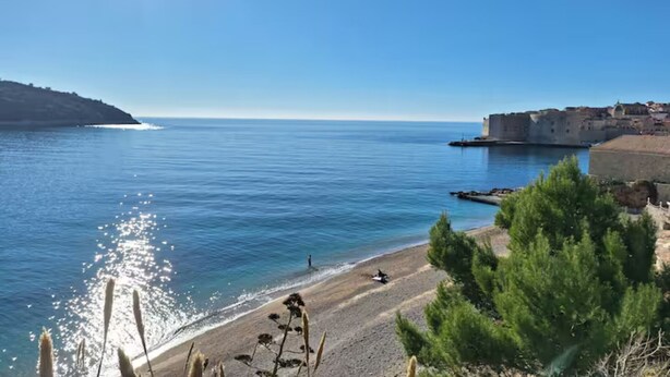 A coastal view with a clear sky, calm sea, and a historic building near the shore.