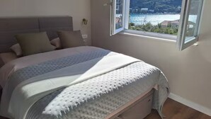 A bedroom with a bed, a window, and a view of a lake and mountains.
