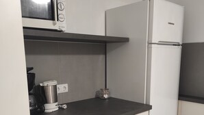 Cocina compacta con microondas, refrigerador y cafetera sobre la encimera.
